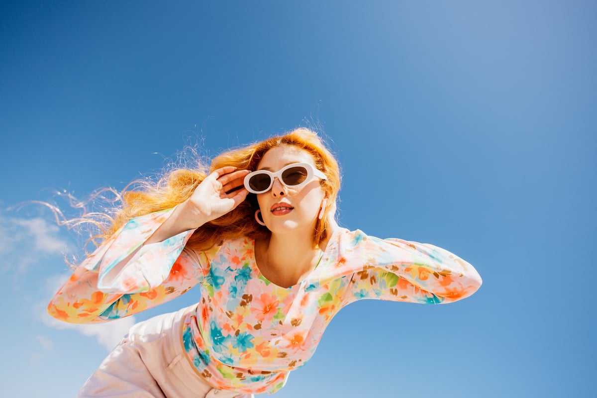 Young woman posing against a bright sky, adjusting sunglasses